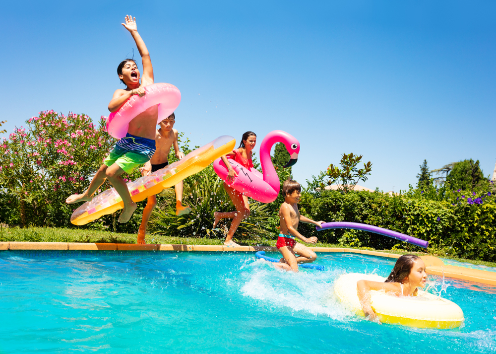 four children jumping into a pool with flotation devices on